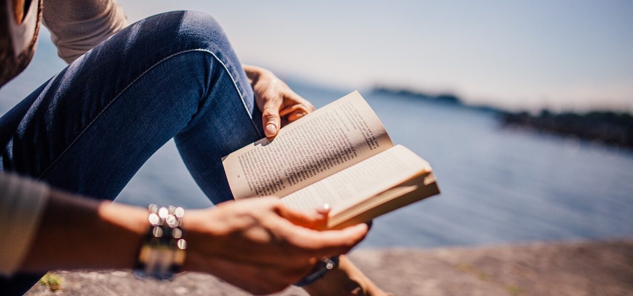 Femme lisant un livre devant un lac, symbolisant le développement personnel.