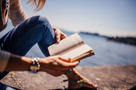 Femme lisant un livre devant un lac, symbolisant le développement personnel.